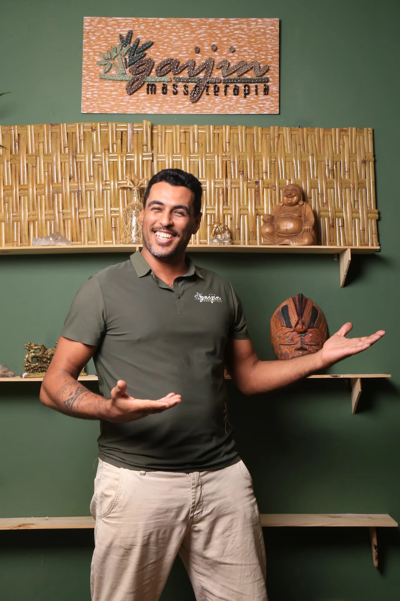Carlos Rodrigues sorrindo com os braços abertos, diante do logo da Gaijin e do painel de bambu